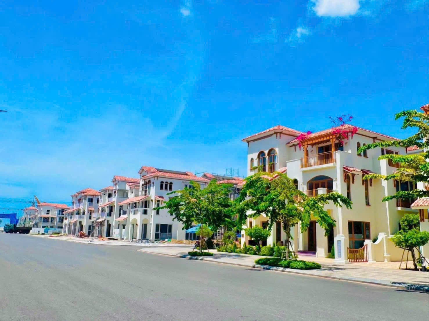Đường nội khu rộng chạy dọc dãy biệt thự trắng đang hoàn thiện dưới bầu trời xanh