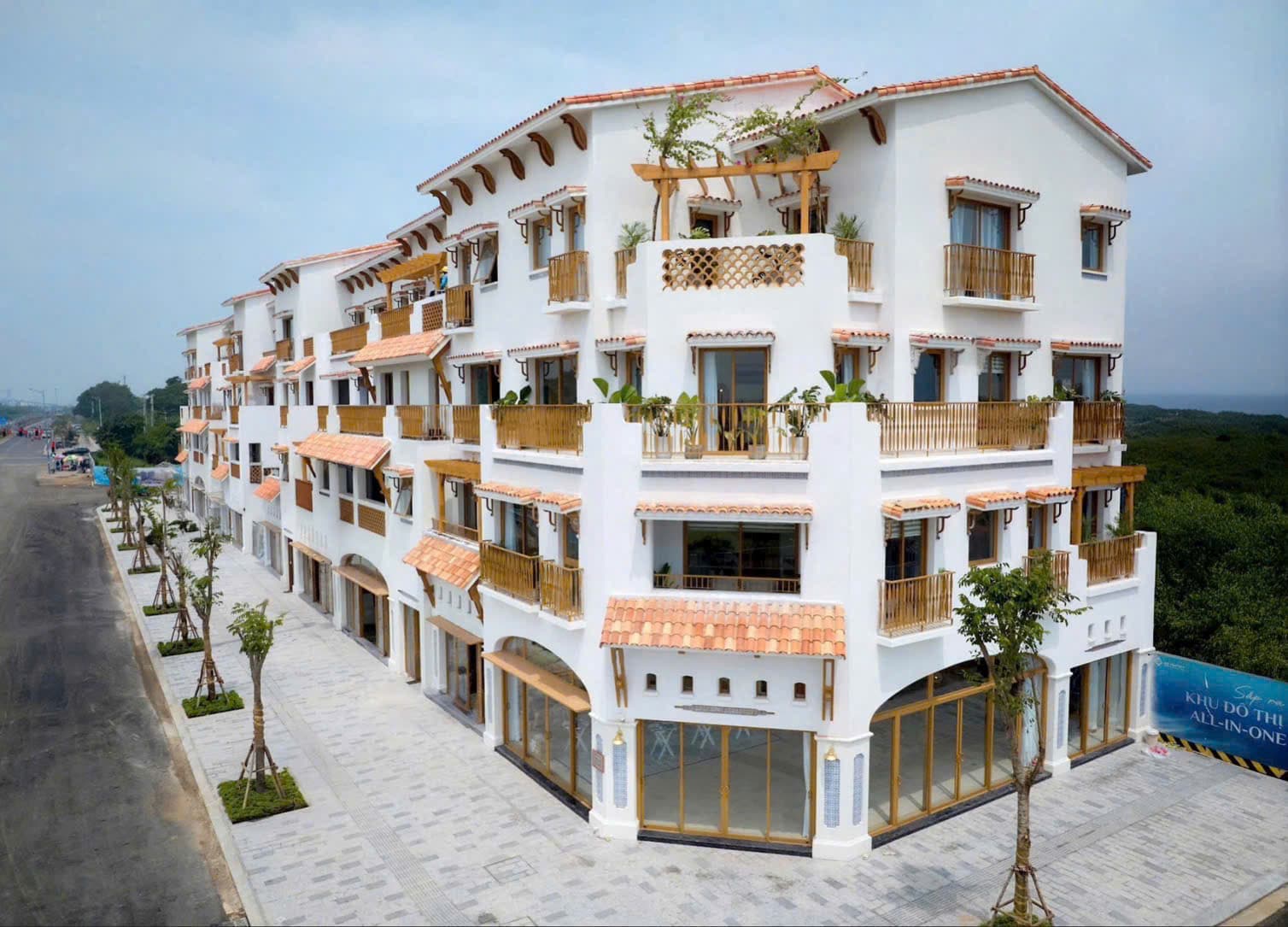 Ảnh flycam dãy shophouse trắng bốn tầng bên đường lớn, rừng cây xanh trải dài phía sau