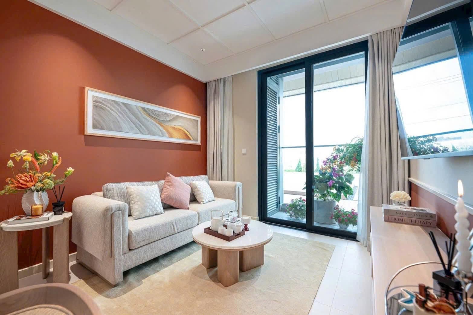 Phòng khách căn hộ mẫu tông cam đất, sofa vải và cửa kính ra ban công