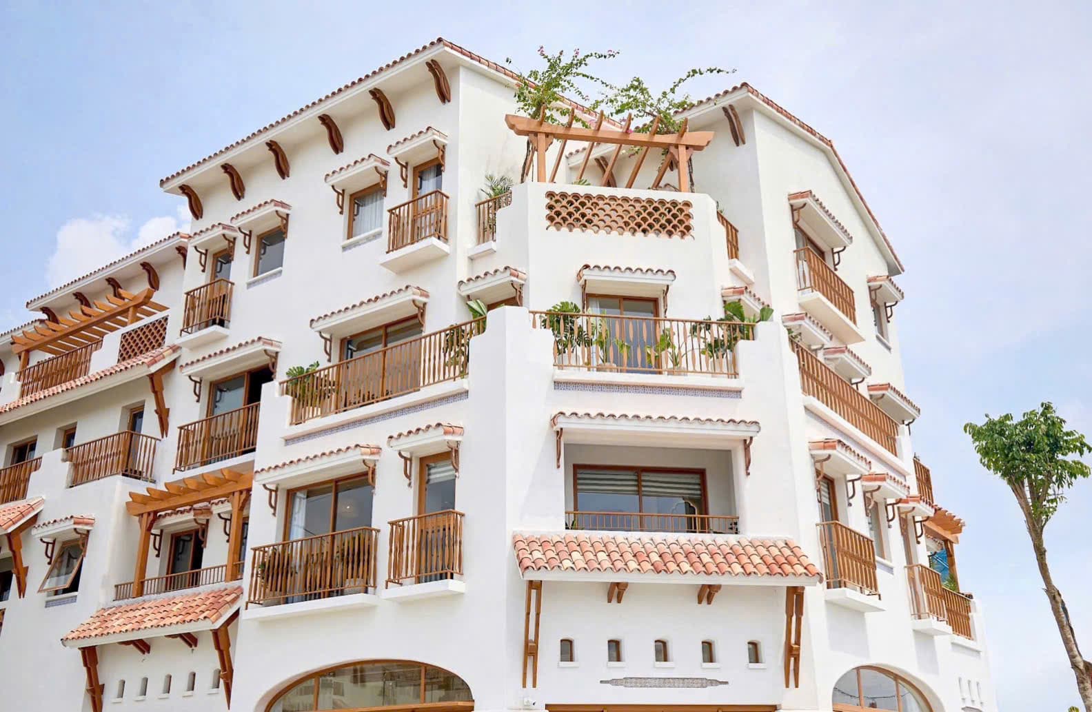 Công trình thấp tầng sơn trắng với ban công gỗ, pergola và mái ngói, nhìn từ dưới lên trời xanh