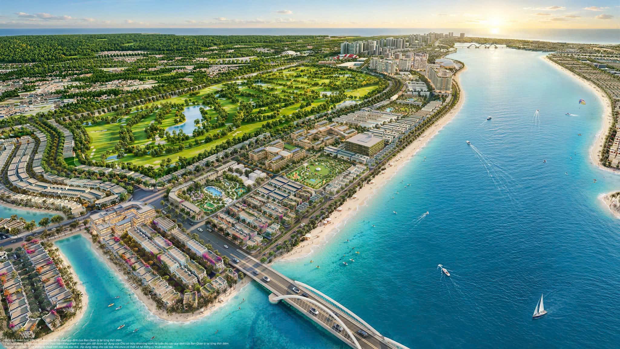 Phoi canh toan khu ban ngay nhin tu tren cao, san golf xanh muot co ho nuoc o giua, day nha thap tang va bai bien cat trang chay dai, cau vom bac qua vinh, bien xanh ngoc phia truoc